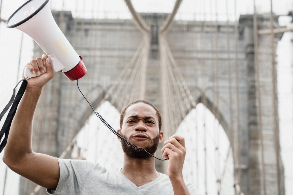Protester with megaphone standing on iconic Brooklyn Bridge.